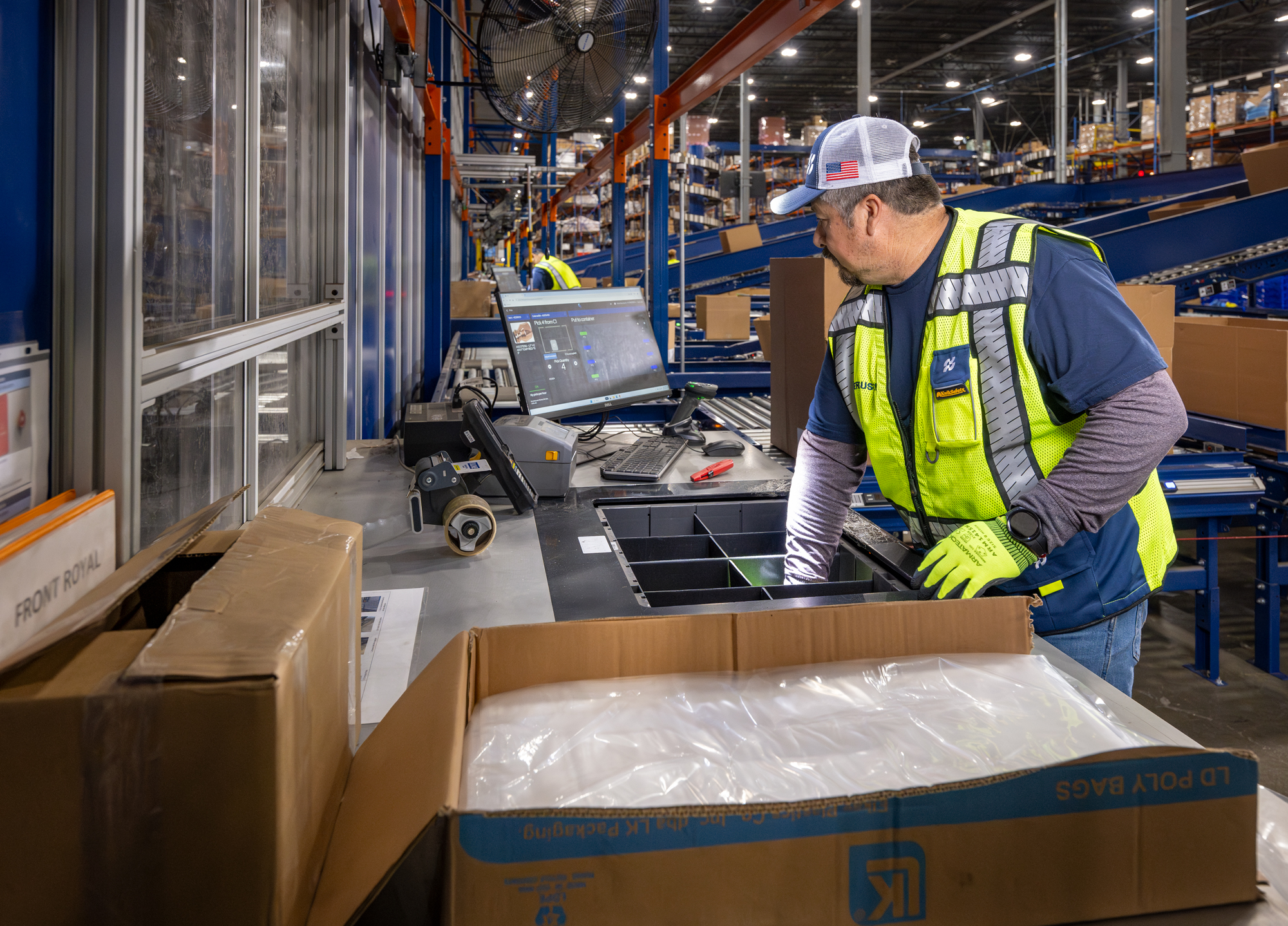 A man in a hi-vis vest packaging supplies with bubble wrap in a cardboard box.